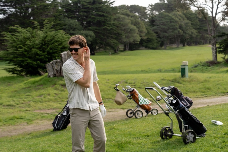 Smiling golfer beside push carts on a tree-lined course