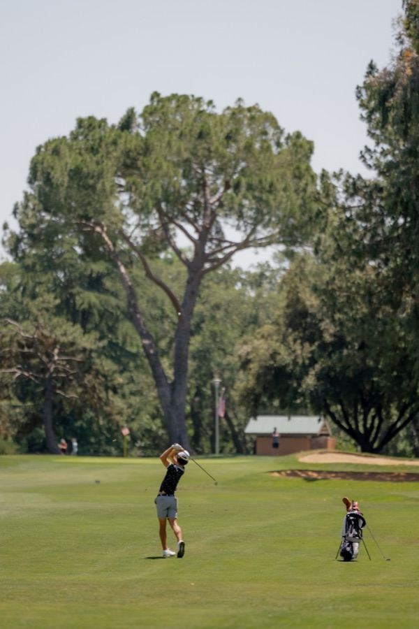 Golfer hitting an approach shot down a tree-lined fairway