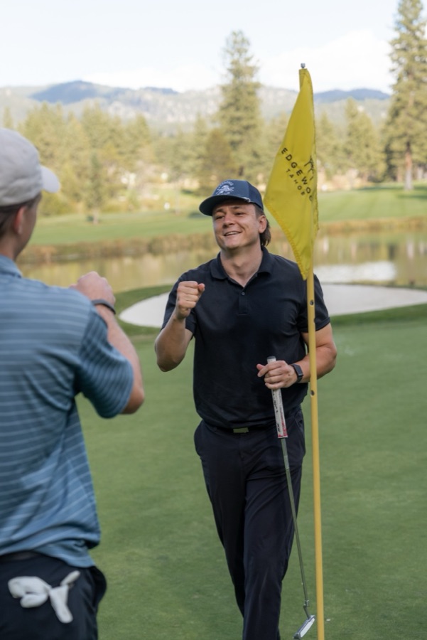 Golfer celebrating with a fist bump beside a yellow flag