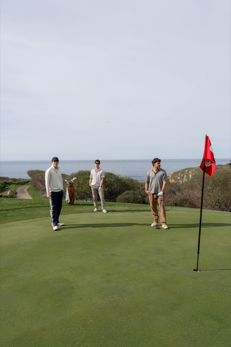 Three golfers on a green above the ocean beside a red flag