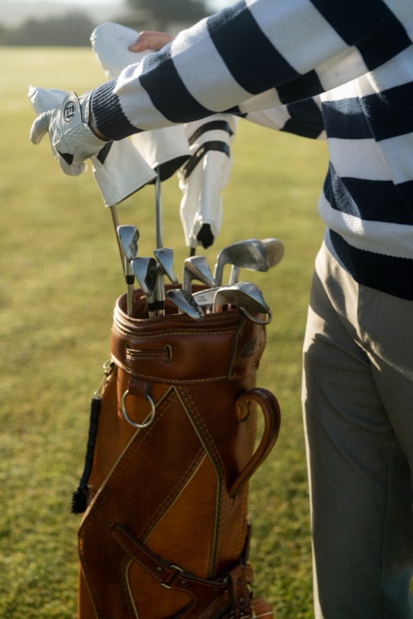 Golfer in a striped sweater pulling clubs from a leather bag