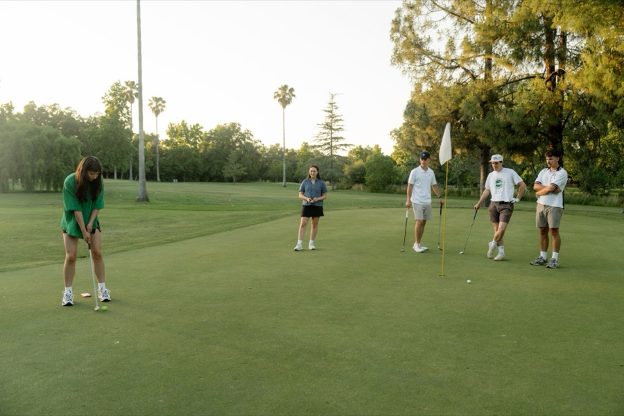 Young golfer putting while friends watch on the green at golden hour