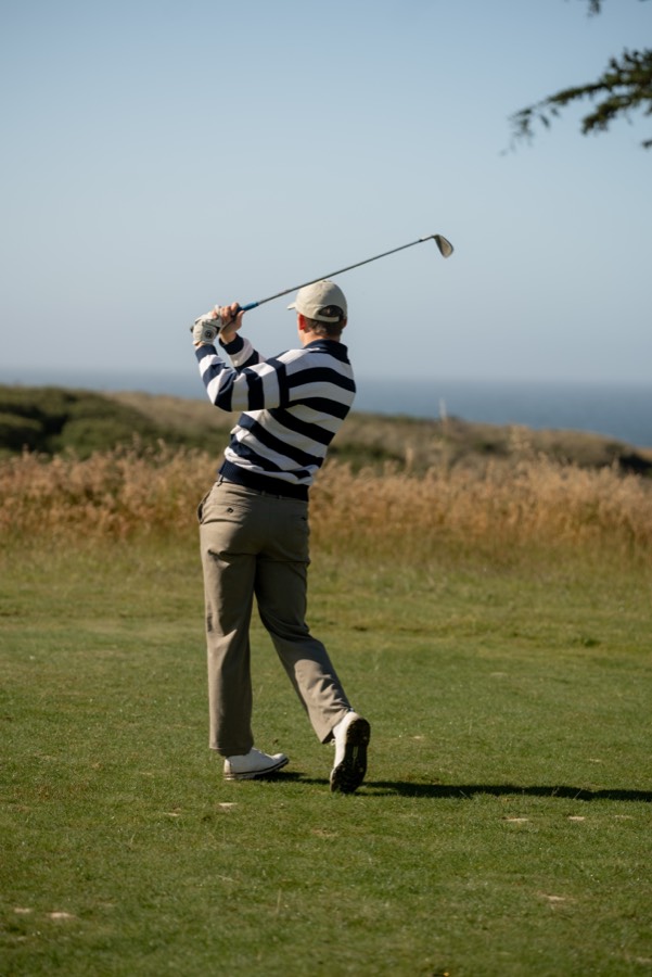 Golfer in a striped sweater finishing a swing above the ocean