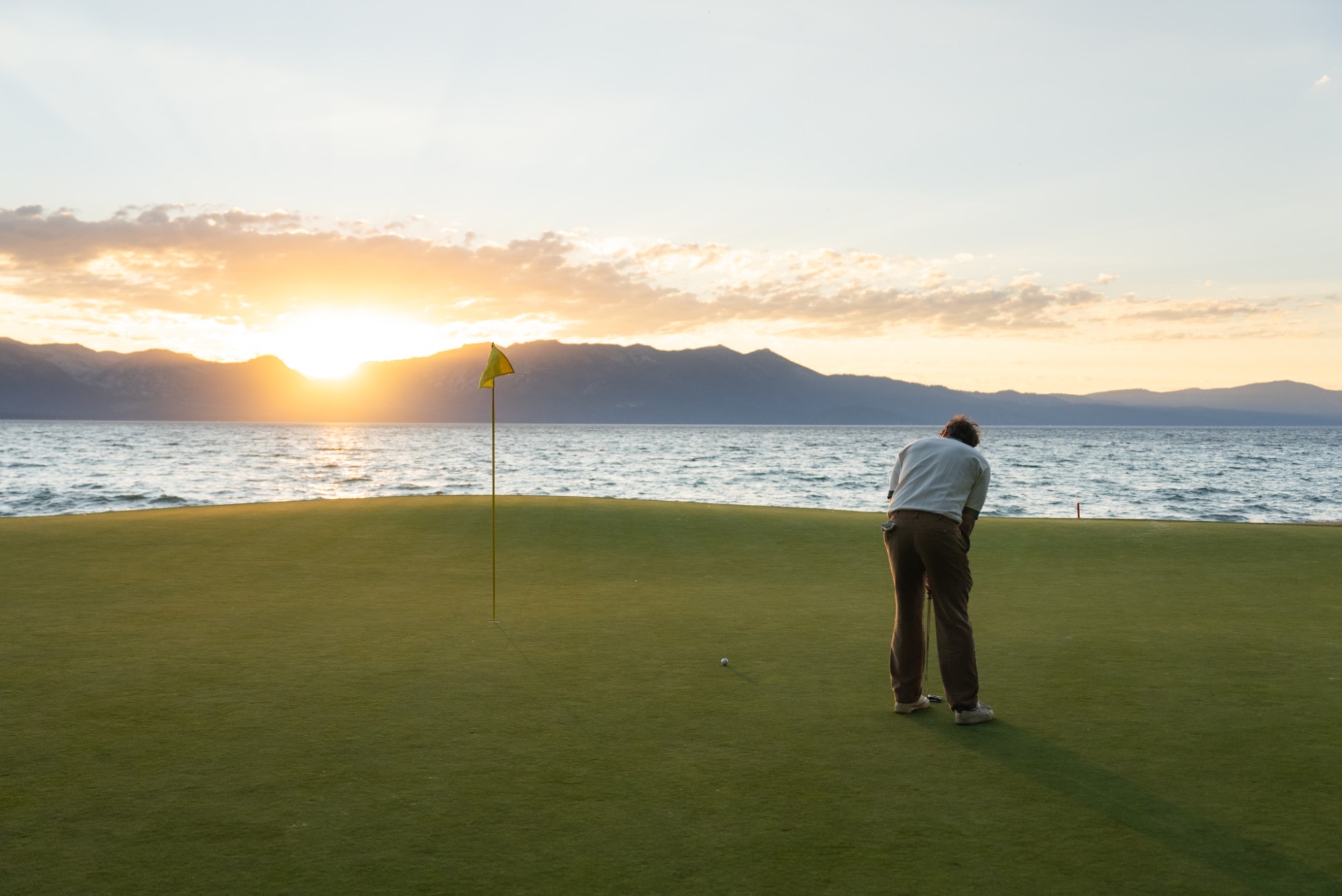Golfer putting on a lakeside green at sunset