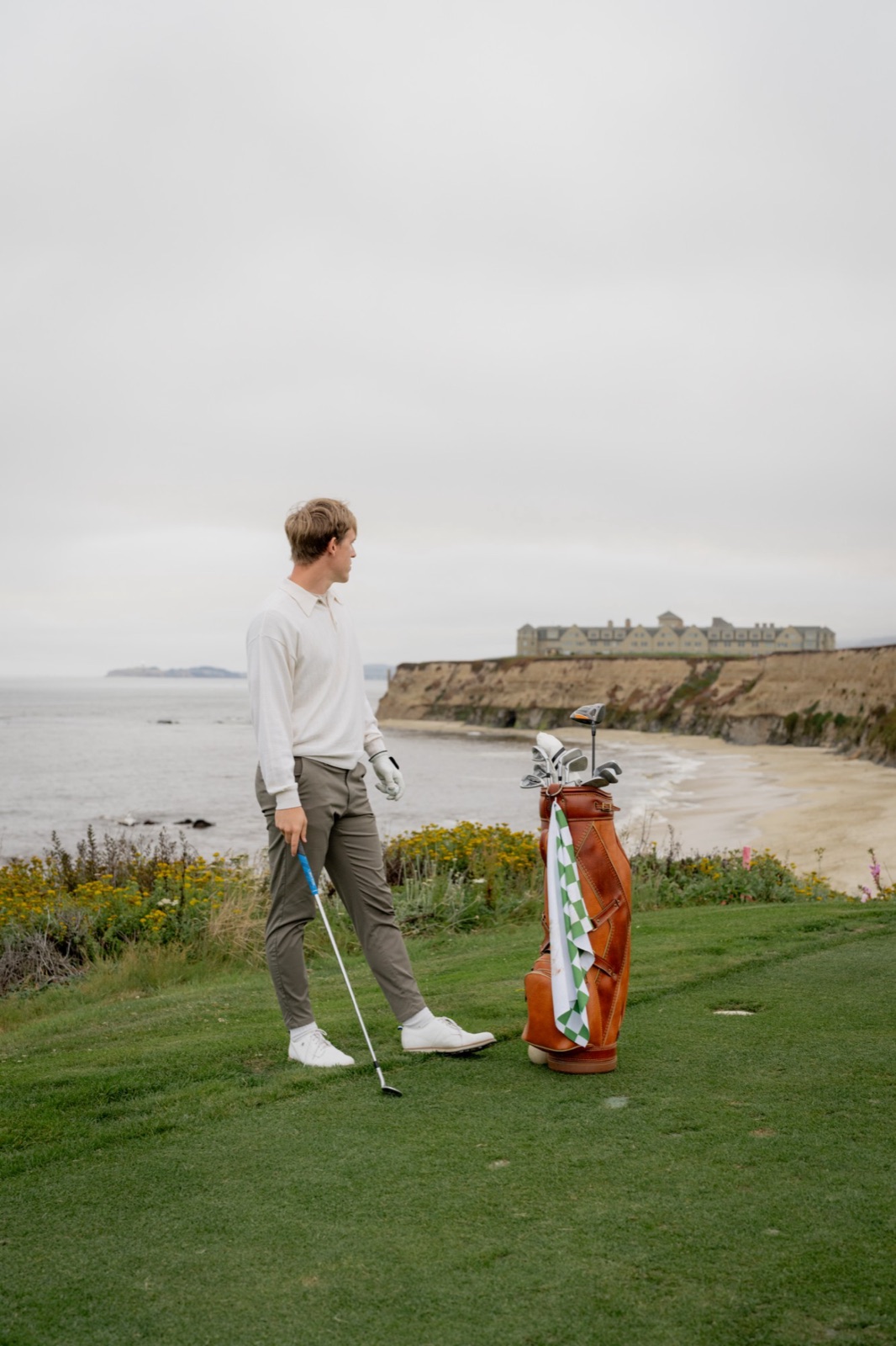 Golfer beside a leather bag on a clifftop tee above the ocean